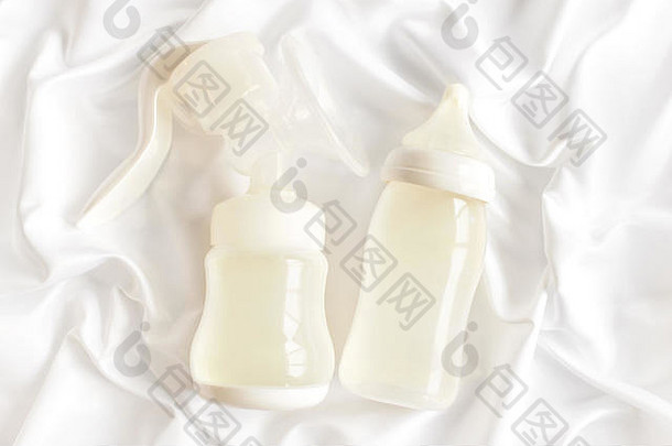 白色丝绸缎子背景上的新生儿奶瓶和手动吸奶器。顶视图。妇幼保健概念。