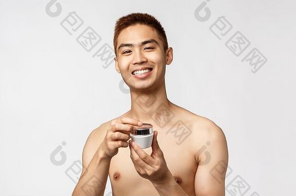 美、人与休闲的概念。帅哥亚洲裸男开护肤霜，笑容可掬，涂抹日常护肤品并微笑