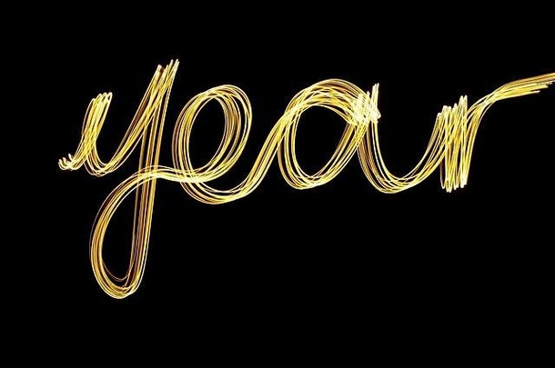 光绘画摄影长曝光黄金金属黄色的光拼写词“年”黑色的背景快乐一年概念