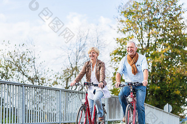 老年夫妇，已婚男女，骑着自行车过桥，享受着闲暇时光