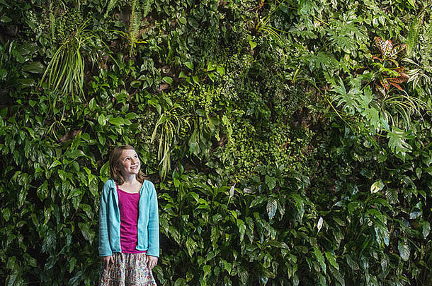 春天的城市城市生活方式一个年轻女孩站在一堵覆盖着蕨类植物和攀缘植物的墙前