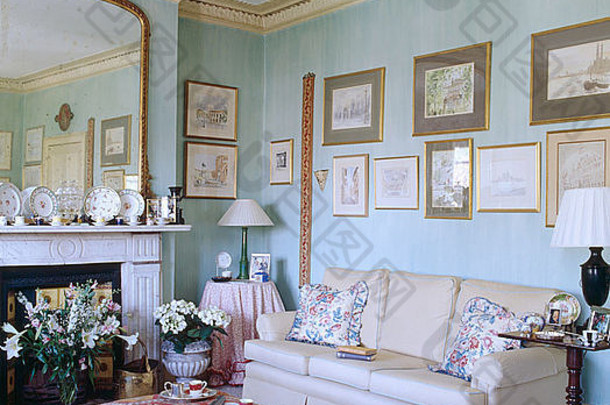 在淡蓝色客厅中，Kelim软垫脚凳和奶油色沙发，墙上的图片上方有华丽的檐口