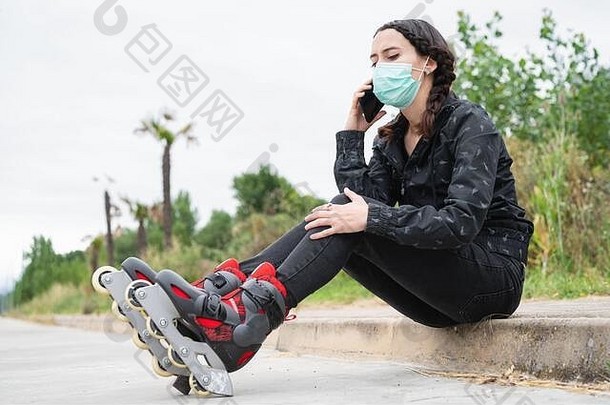 女人保护脸面具辊滑冰暂停坐着街移动电话冠状病毒流感大流行爆发城市女孩会说话的电话穿辊溜冰鞋