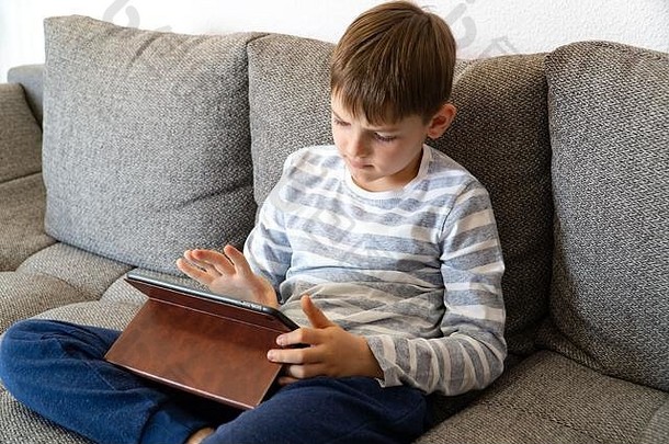 年轻的男孩思<strong>考前</strong>面平板电脑距离学习在线教育可爱的高加索人男孩家庭作业首页检疫