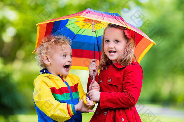 男孩女孩玩多雨的公园孩子们色彩斑斓的彩虹伞防水夹克外套玩雨