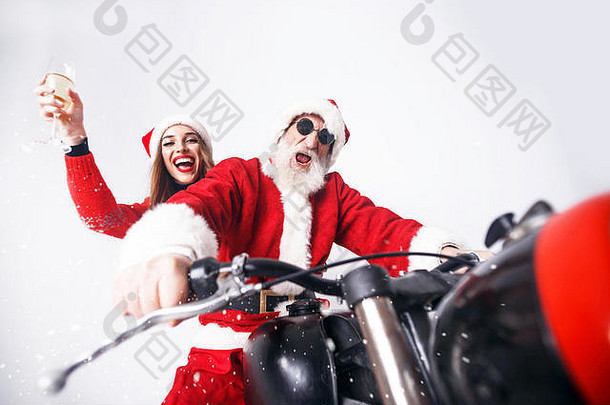 圣诞老人老人白色胡子穿sungasses年轻的夫人老人穿圣诞老人他红色的毛衣太阳镜骑摩托车下雪夫人老人喝香槟一年圣诞节假期记忆礼物购物折扣商店雪少女圣诞老人老人化妆发型狂欢节