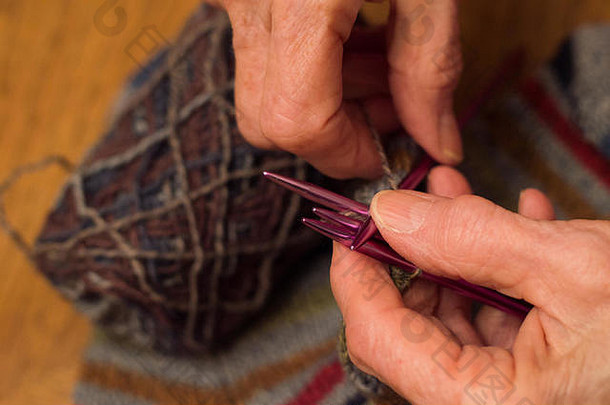上了年纪的女人的手针织樱红色针一束纱完成了袜子表格背景