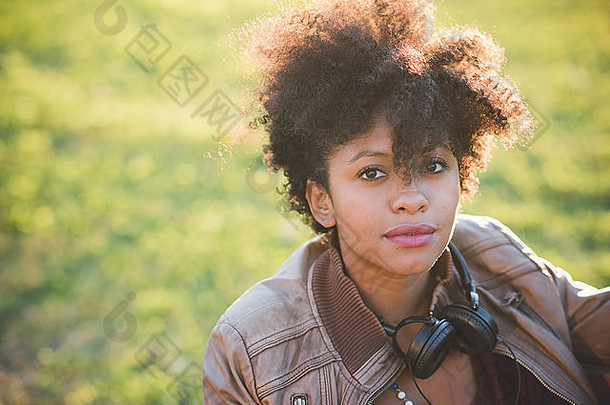 肖像年轻的美丽的黑色的卷曲的头发非洲女人摆姿势坐着板凳上公园相机持有智能<strong>手机</strong>新鲜青年概念背光