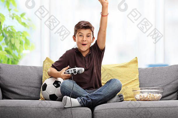 快乐的孩子玩足球视频游戏庆祝目标拳头空气坐着灰色的沙发