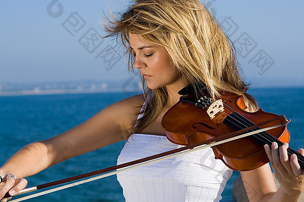 美丽的年轻的女人玩小提琴海滩