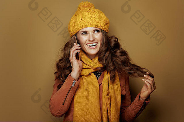 快乐年轻的女人黄色的贝雷帽围巾会说话的细胞电话米色背景