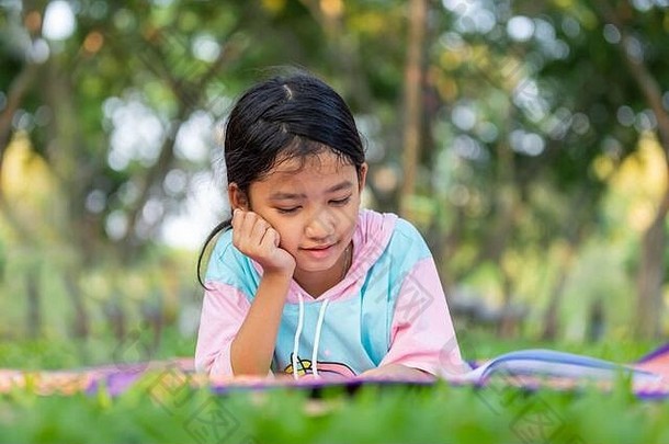亚洲女孩躺把手下巴微笑草坪上花园孩子阅读书假期