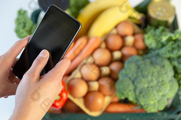 食物交付服务女人持有智能手机前面盒子食品杂货