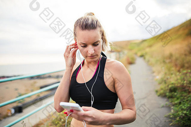 年轻的运动女人跑步者耳机智能手机站海边