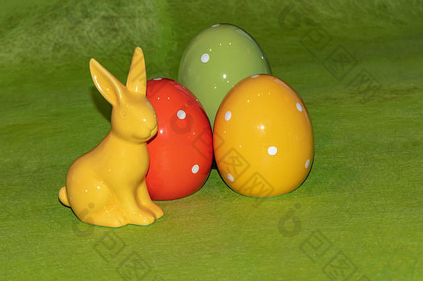 色彩斑斓的陶瓷复活节鸡蛋复活节兔子前面绿色背景