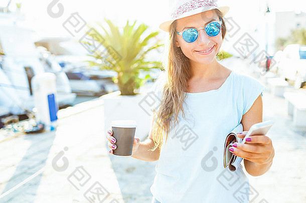 快乐年轻的时尚的女人喝外卖咖啡走海滨早....