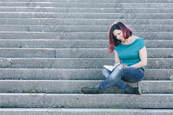 英俊的红色头发的人年轻的女人坐着石头楼梯阅读书概念放松自然