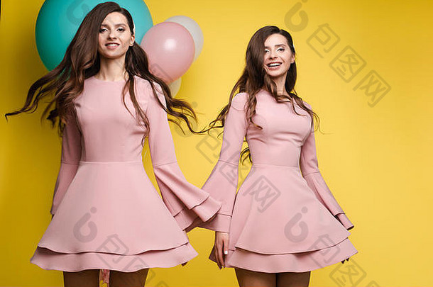 可爱的浅黑肤色的女人双胞胎粉红色的礼服黄色的背景