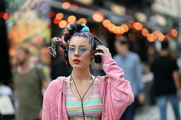 时尚很酷的时髦的女孩耳机听音乐穿色彩斑斓的粉红色的毛衣花俏的太阳镜街酒吧酒吧unrecognis