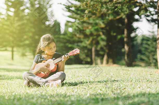 年轻的快乐亚洲女孩玩尤克里里吉他公园阳光明媚的早....爱好宁静概念