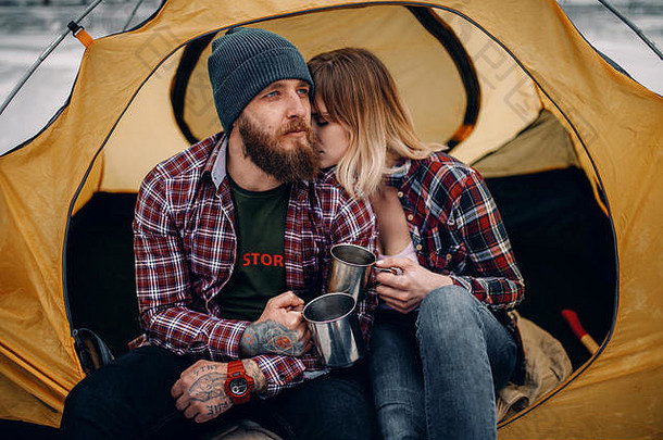 年轻的夫妇坐在黄色的旅游帐篷饮料热茶杯子冬天徒步旅行