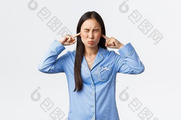 困扰愚蠢的亚洲女孩蓝色的睡衣讨厌困扰声音关闭耳朵眼睛扮鬼脸不满意抱怨大声噪音心烦意乱