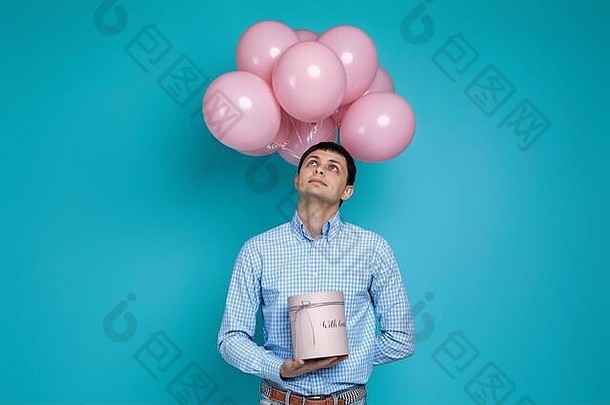 快乐高加索人男人。持有礼物盒子柔和的粉红色的空气气球孤立的蓝色的背景生日聚会，派对