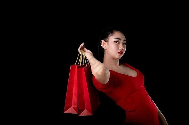 肖像美丽的年轻的亚洲女人穿红色的衣服持有信贷卡购物袋黑色的背景出售概念