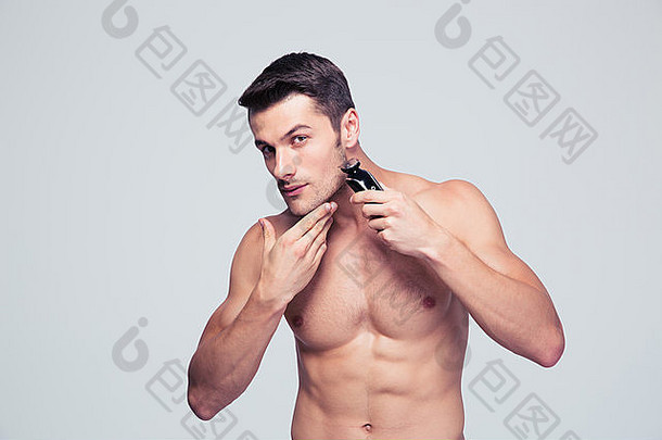 肌肉发达的年轻的男人。剃须电剃须刀灰色的背景相机