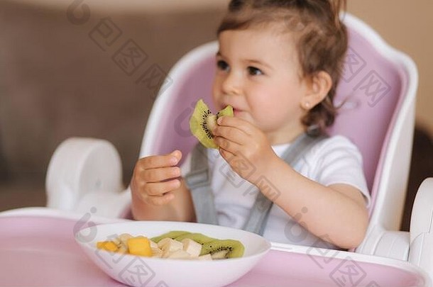 肖像快乐孩子吃猕猴桃高椅子健康的营养孩子们