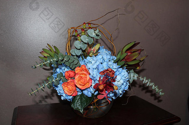 花安排蓝色的绣球花兰花珊瑚玫瑰桉树玫瑰果玻璃花瓶固体背景