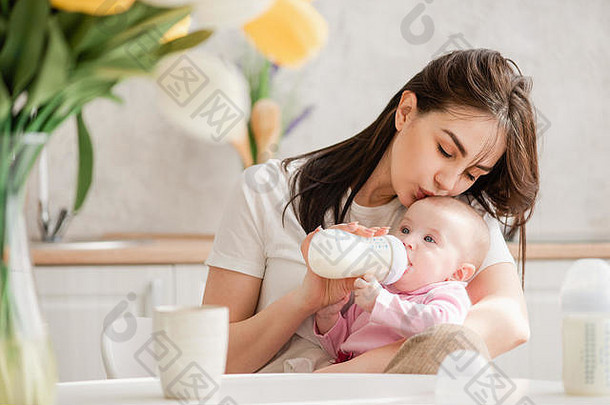 年轻的女人吻婴儿喝牛奶