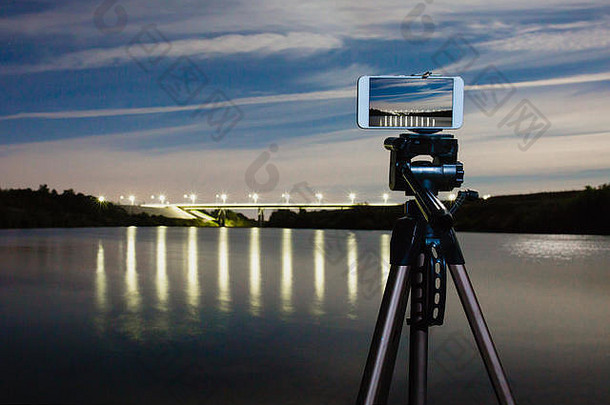 智能手机专业相机三脚架捕捉晚上景观很多灯反映了表面水