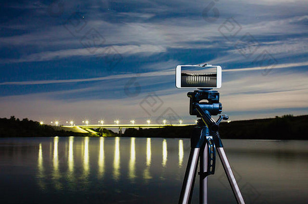 智能手机专业相机三脚架捕捉晚上景观很多灯反映了表面水