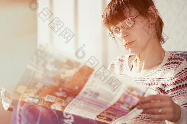 女人放松阅读杂志温暖的阳光照射的厅的首页