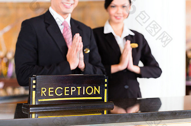 中国人亚洲接待团队奢侈品酒店前面桌子上欢迎客人典型的手势标志好服务