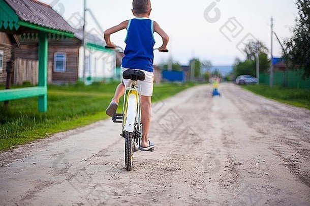 年轻的男孩骑自行车污垢路后视图