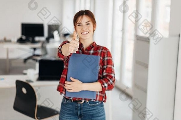 休闲现代年轻的工作申请人给拇指手势成功站持有微笑相机宽敞的办公室