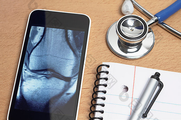 技术医疗保健智能手机显示x射线扫描膝盖声听诊器记事本笔医生办公室桌子上