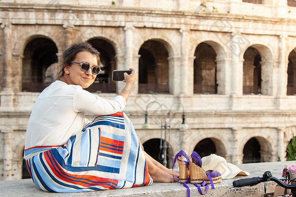美丽的年轻的女人采取图片智能手机坐着前面罗马圆形大剧场罗马日落