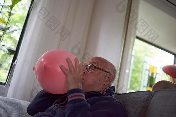 上了年纪的退休男人。吹大心形状的粉红色的气球装修房间生日聚会，派对