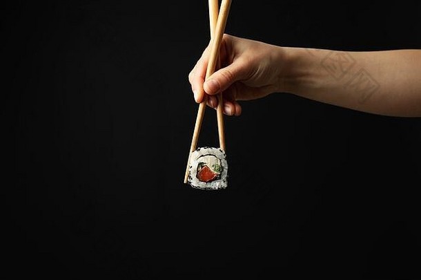 女手筷子持有寿司卷黑色的背景日本食物