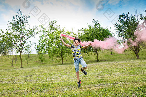年轻的男孩运行落后于粉红色的烟耀斑绿色春天公园花园