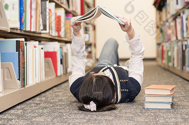年轻的女孩学生铺设图书馆地板上阅读堆栈书