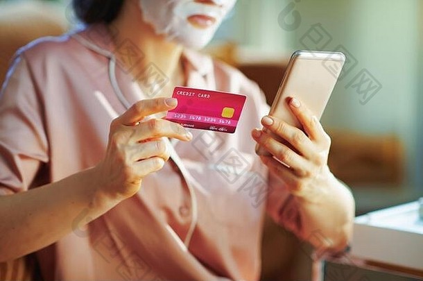 特写镜头现代女人睡衣白色表面部面具脸持有智能手机信贷卡浏览美化妆品在线电子商务