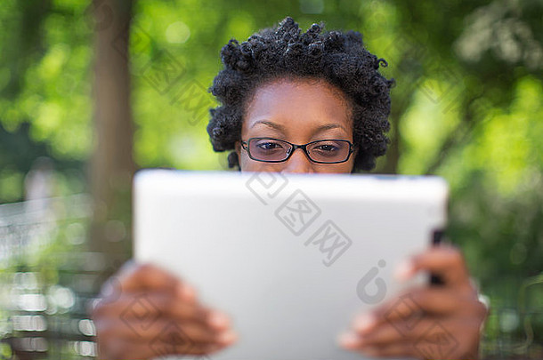 年轻的女人公园持有阅读数字平板电脑