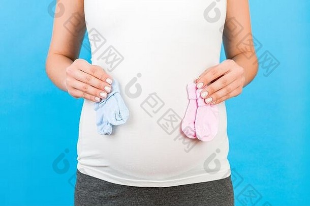 裁剪肖像怀孕了女人首页服装持有婴儿粉红色的蓝色的袜子肚子蓝色的背景男孩女孩孩子