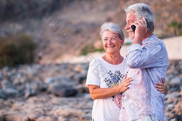 概念假期技术旅游旅行人快乐高级夫妇细胞电话电话卵石海滩笑在开玩笑白色头发