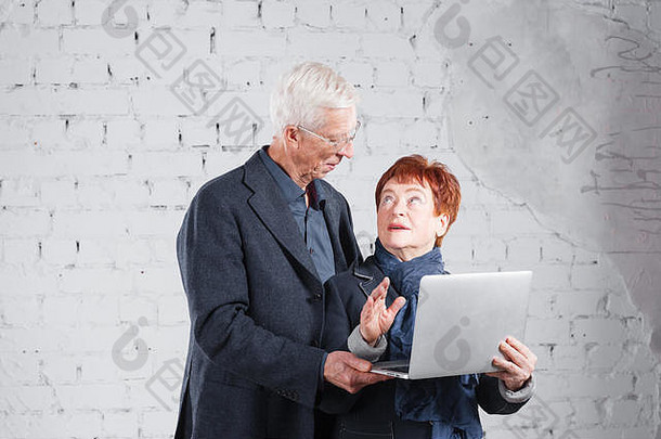 人持有移动PC沟通互联网快乐微笑爷爷奶奶夫妇站拥抱孤立的白色砖背景