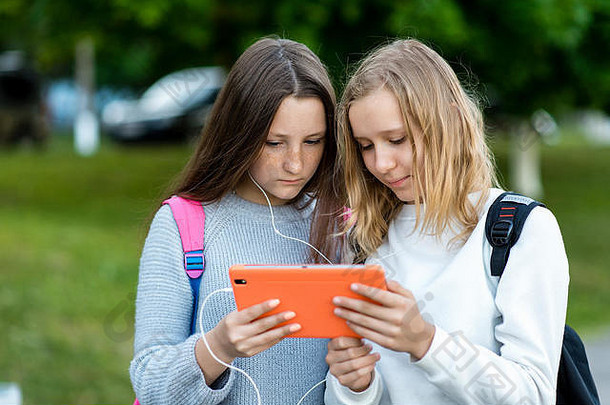 十几岁的女孩夏天公园学校手持有平板电脑手表电影听音乐概念朋友朋友看视频互联网社会网络